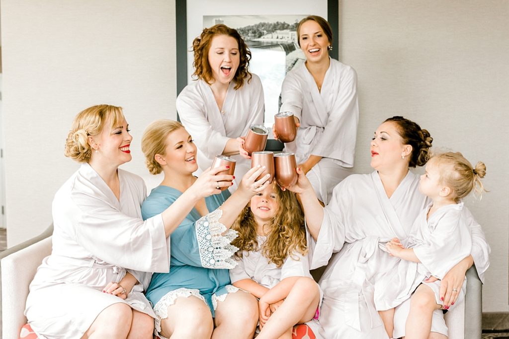 bridesmaids in white silk robes with bride in blue silk lace robe drinking champagne out of rose gold yeti wine glasses