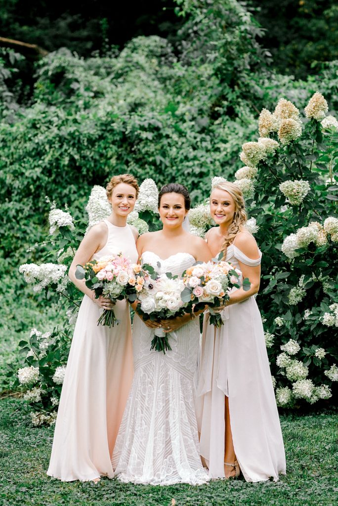 Bride with two bridesmaids in front of flower bush